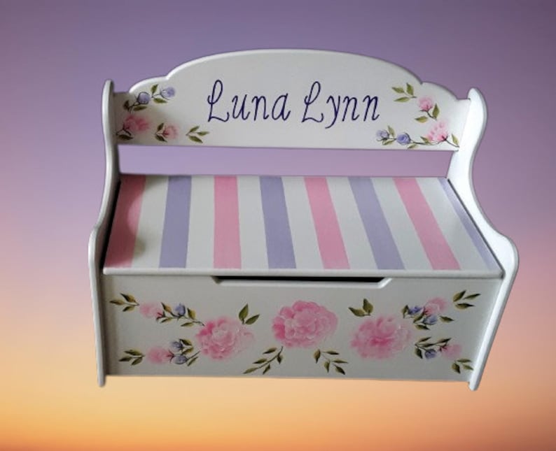 May include: White wooden storage bench with a pink and purple striped seat and floral painted design. The bench is personalized with the name "Luna Lynn".