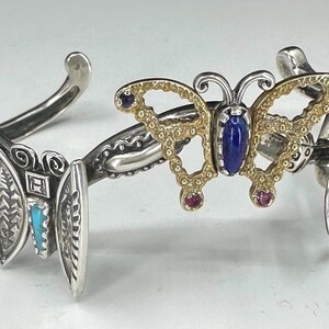 Puede incluir: Pulsera de plata con brazalete con mariposa y otros elementos decorativos. La mariposa tiene alas doradas con piedras preciosas azules y rojas. Otros elementos incluyen turquesa y naranja.
