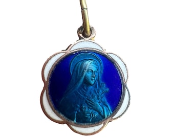 May include: A small, vintage pendant featuring a religious image. The pendant has a blue and white enamel design with a gold-colored metal frame. The image depicts a woman with a halo, holding a cross and flowers.
