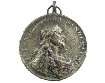 Puede incluir: Colgante antiguo de bronce con un retrato de perfil. El colgante circular tiene un lazo para colgar y letras en relieve alrededor del borde. La superficie tiene un aspecto desgastado, lo que sugiere edad y uso.