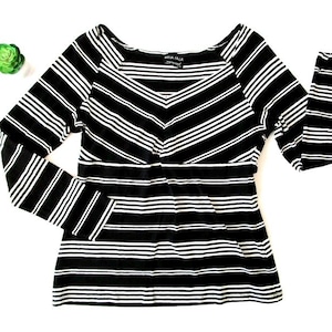 May include: A black and white striped long-sleeved top. The top has a scoop neckline and a chevron design on the bodice. The sleeves are long and fitted. The brand name "Nina Talla" is visible on the neckline.