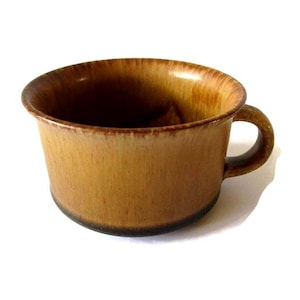 May include: A brown ceramic mug with a handle. The mug has a wide, slightly flared rim and a dark brown base. The exterior has a textured appearance with variations in colour, ranging from light to dark brown.