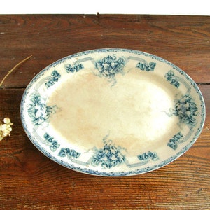 May include: Oval serving platter with a cream-colored center and a blue floral border. The blue floral design is repeated around the edge of the platter. The platter is set on a dark wooden surface.