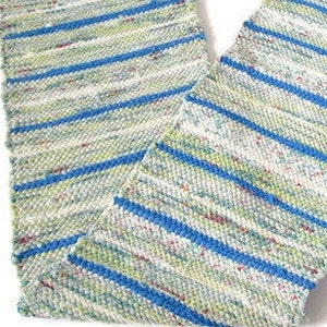 May include: A woven fabric runner featuring a repeating pattern of horizontal stripes in bright blue, light green, and white. The white sections contain small, multicolored flecks of red, blue, and green fiber throughout the textured material.