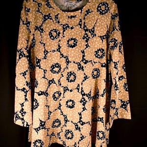 Può includere: Una maglia a maniche lunghe con un motivo floreale ripetuto in beige e nero. Il capo presenta uno scollo rotondo e una vestibilità ampia e fluida. Il tessuto è ricoperto da grandi forme di fiori stilizzati con centri scuri e petali beige.