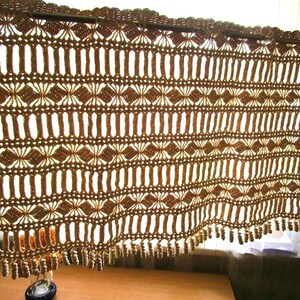 以下が含まれることがあります： 茶色の鉤針編みカーテン。ひし形と縦線の繰り返し模様。カーテンはスカラップのトップエッジと下部にフリンジが付いています。デザインは光が透過するように設計されています。
