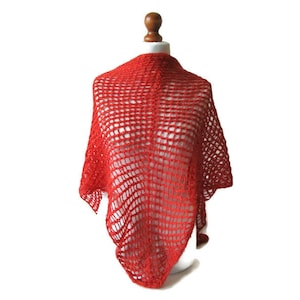 May include: A vibrant red, open-weave shawl draped over a mannequin. The shawl's design features a grid-like pattern, creating a textured appearance. The bright red color is consistent throughout the fabric, offering a bold and eye-catching accessory.