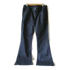 Peut inclure: Jean en denim bleu foncé avec une coupe évasée. Le jean est suspendu à un cintre en bois. Le pantalon a une fermeture à bouton et à glissière, et des poches. Le jean est de style classique.