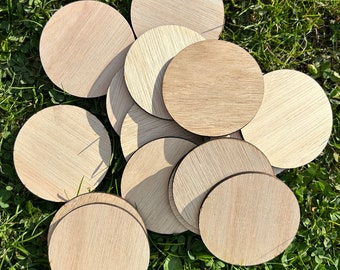 May include: A pile of round, unfinished wooden circles, likely for crafts, arranged on a bed of green grass.