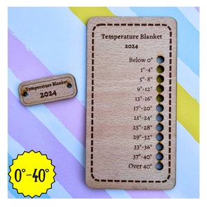 May include: A wooden temperature blanket gauge with a brown border and holes for marking temperatures from below 0 degrees Fahrenheit to over 40 degrees Fahrenheit. The gauge is labeled "Temperature Blanket 2024".