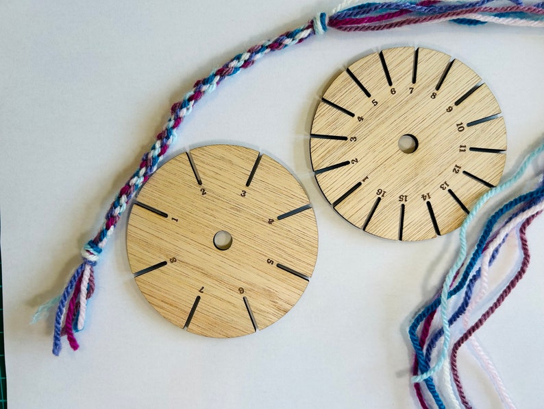 Op de afbeelding: Twee ronde houten gereedschappen met sleuven voor touw, genummerd van 1 tot 15. Een veelkleurig touw is om de gereedschappen gewikkeld en een gevlochten touw bevindt zich aan de linkerkant van de afbeelding.