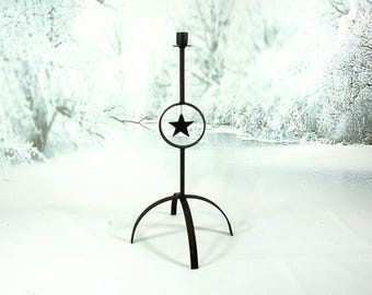 May include: Black metal candle holder with a star design. The candle holder has a circular frame with a star in the center, supported by a tall stem and a three-legged base. The candle holder is designed to hold a single candle.