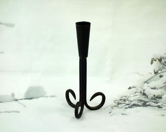 May include: A black metal candlestick holder with a tall, slender stem and a flared top. The base features three curved legs. The candlestick holder is approximately 8 inches tall.