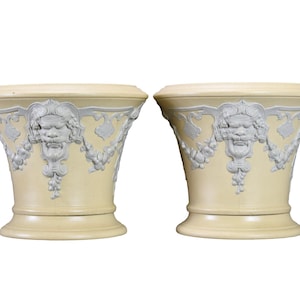 May include: A pair of cream-coloured ceramic planters with white raised designs. Each planter features a lion's head with floral accents.