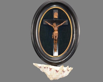 Puede incluir: Un marco ovalado negro con un crucifijo dorado y una figura de Jesucristo. El marco está colgado sobre una concha blanca.