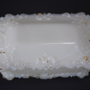 Puede incluir: Caja de porcelana blanca para alhajas con un dise&ntilde;o floral ornamentado y en relieve alrededor de los bordes. La caja tiene un borde dorado.