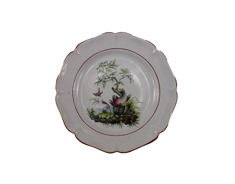 May include: White ceramic plate with a red rim and a hand-painted design of a bird perched on a branch with a butterfly in flight. The design is in shades of green, blue, pink, and yellow.
