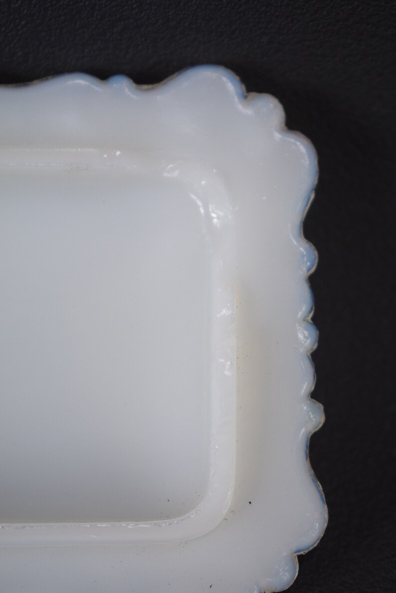 Puede incluir: Plato de mantequilla de vidrio de leche blanco con borde festoneado y borde azul.