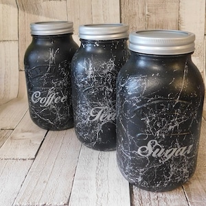 May include: Three black glass jars with silver lids and white crackle paint. The jars are labelled "Coffee", "Tea", and "Sugar".
