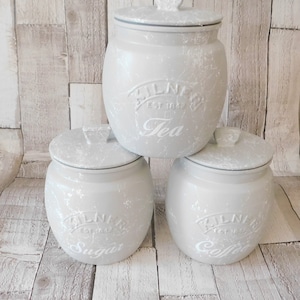 May include: Three grey ceramic canisters with white lids and white lettering. The canisters are labelled "Tea", "Sugar", and "Coffee".