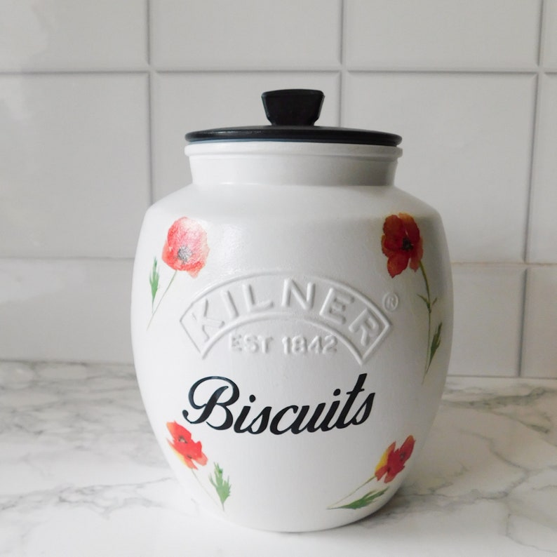 May include: White ceramic biscuit jar with a black lid and poppy flower illustrations. The jar features the embossed "Kilner Est 1842" logo and the word "Biscuits" in a black script font.