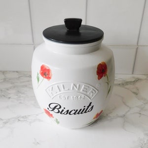 May include: White ceramic biscuit jar with a black lid and handle. The jar is decorated with red poppy flowers and the word "Biscuits" in black script. The jar has the "Kilner Est 1842" logo.