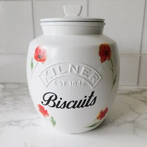 May include: White ceramic biscuit jar with a lid, adorned with red poppy flower illustrations. The jar features the word "Biscuits" in black script and the embossed "Kilner Est 1842" logo.