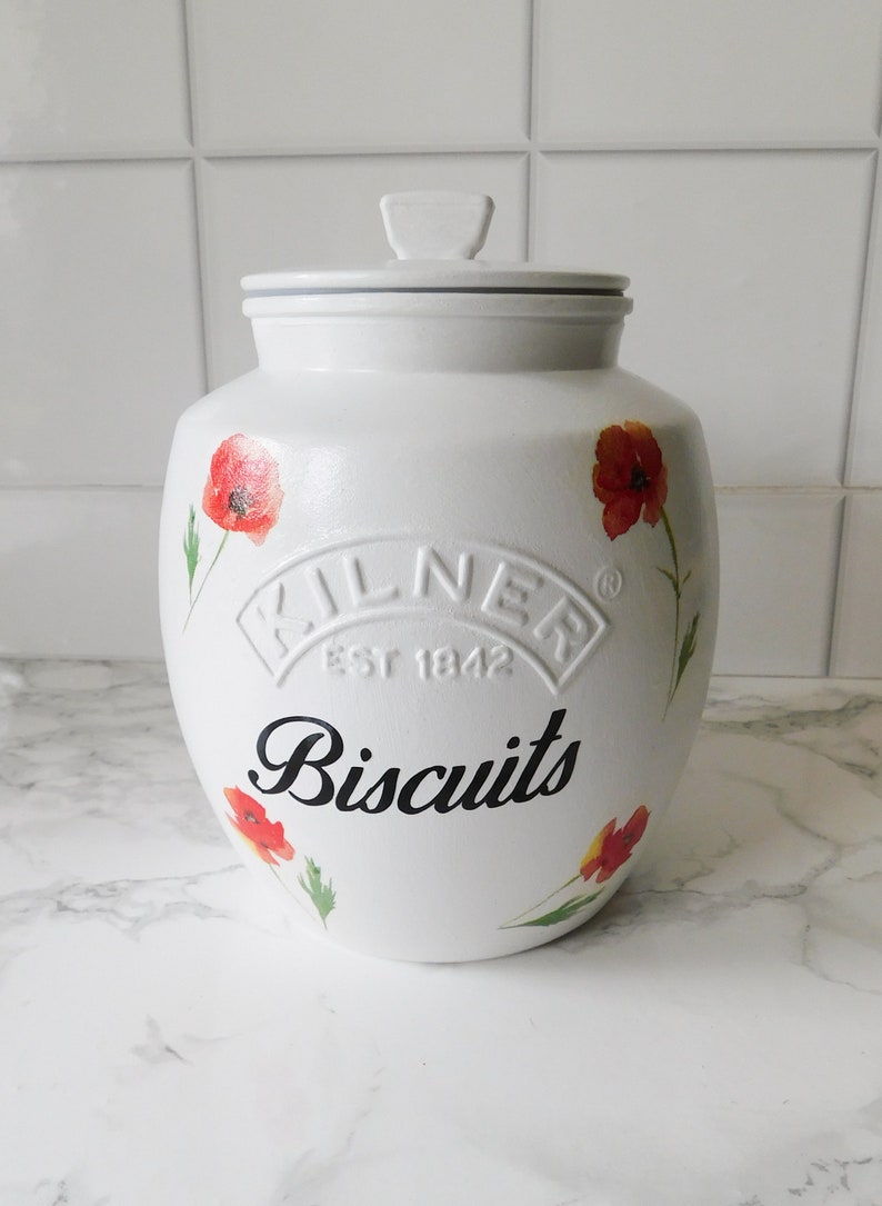 May include: White ceramic biscuit jar with a lid, adorned with red poppy flower illustrations. The jar features the word "Biscuits" in black script and the embossed "Kilner Est 1842" logo.
