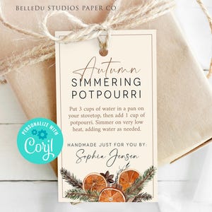 May include: A gift tag with the text "Autumn Simmering Potpourri" and instructions. The tag is cream-colored with a brown border and features dried orange slices and greenery. The gift is wrapped in brown paper and tied with twine.
