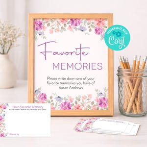May include: A wooden framed sign with the words "Favorite Memories" in purple script and block letters. The sign is decorated with watercolor floral elements in pink, purple, and blue. A glass jar with pencils and memory cards are also present.