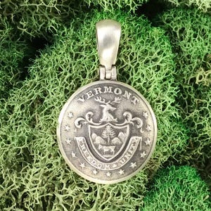May include: Silver pendant featuring the state seal of Vermont. The seal depicts a green pine tree, a cow, and a deer with antlers. The words "Vermont", "Freedom & Unity", and "1777" are inscribed around the seal.
