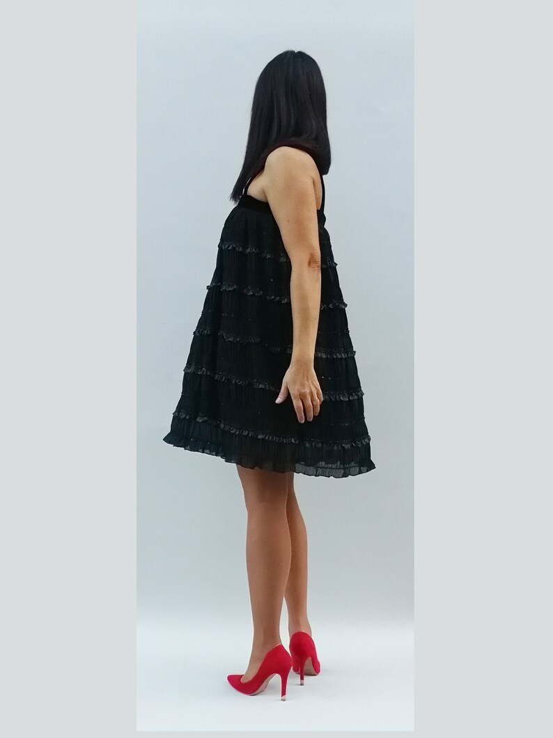 May include: A black tiered dress with a ruffled hem. The dress is sleeveless and has a scoop neck. The model is wearing red high heels.