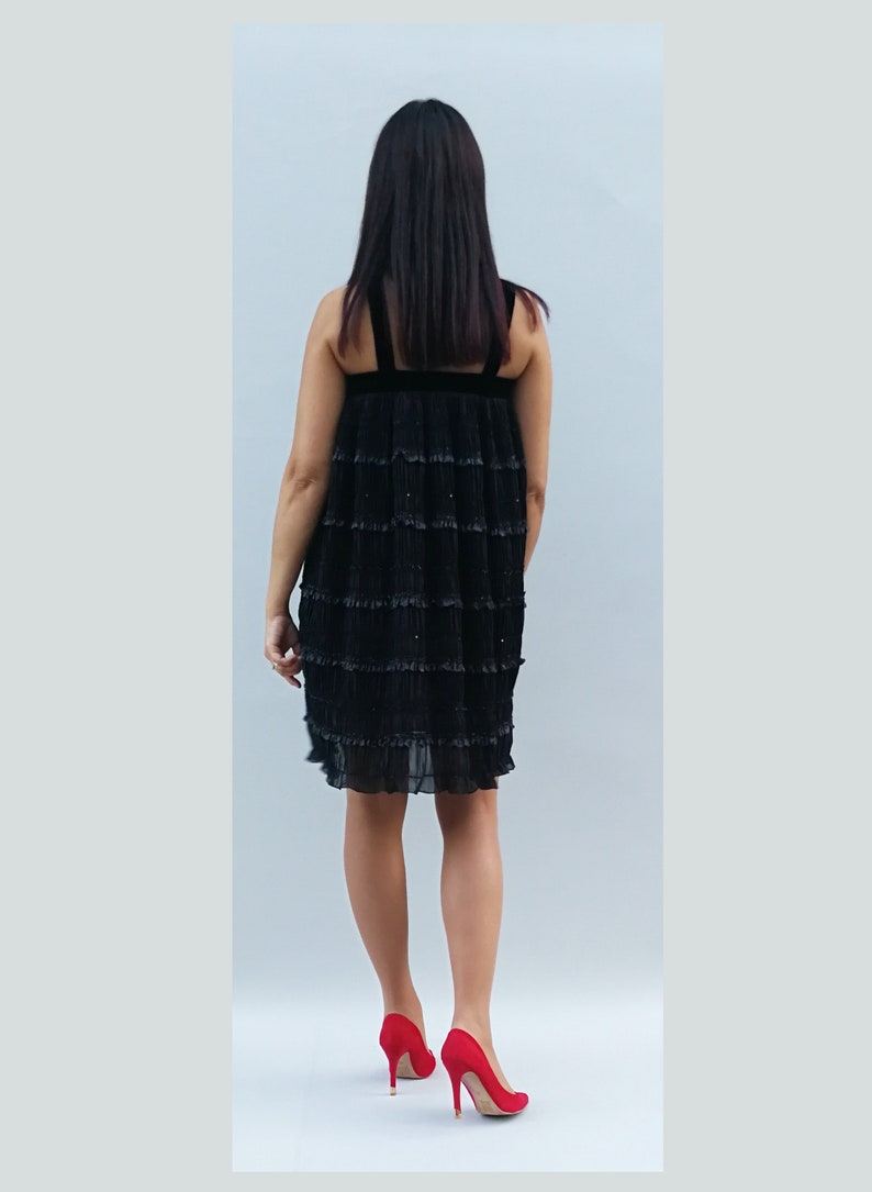 May include: A black tiered dress with a velvet waistband. The dress is made of a sheer fabric with a ruffled hem. The model is wearing red high heels.