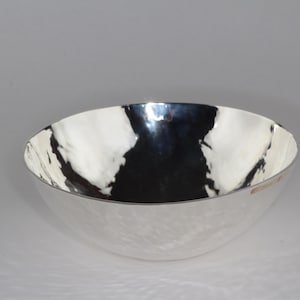 Op de afbeelding: Een zilveren kom met een gehamerde afwerking. De kom is rond en heeft een glad, reflecterend oppervlak.