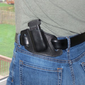 May include: A black leather holster with a gun inside, worn on a person's waist with a black belt.