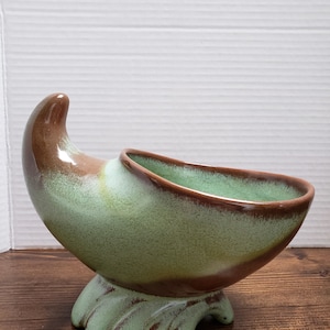 May include: A green and brown glazed ceramic bowl shaped like a cornucopia with a footed base.