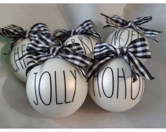 May include: Five white Christmas ornaments with black and white checkered ribbon bows. The ornaments are decorated with the words "CHEER", "JOLLY", "HO HO HO", "MERRY", and "NOEL".