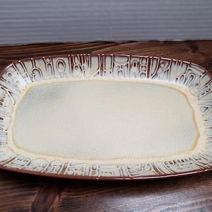 May include: A rectangular ceramic serving platter with a brown rim and a white center. The rim has a raised design of geometric shapes in a light brown color.