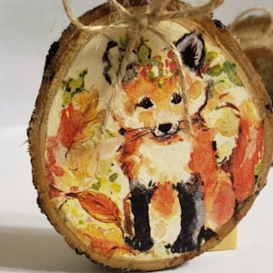 May include: A wooden slice with a printed image of a fox wearing a floral crown. The slice is tied with twine and has a rustic, autumnal feel.