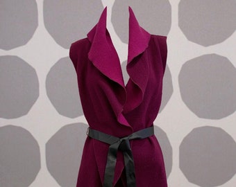 May include: A sleeveless, burgundy-colored, ruffled vest with a black belt. The vest has a wide, ruffled collar and a loose, flowing fit.