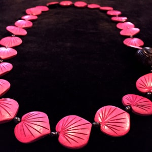 Puede incluir: Un collar de cuentas de madera tallada en forma de coraz&oacute;n rosa. El collar est&aacute; encordado en un cord&oacute;n negro y tiene una cuenta de madera negra en el cierre.