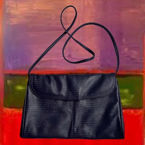 May include: A navy blue shoulder bag with a textured, reptile-like pattern. The bag has a flap closure and a long, thin strap. The background features an abstract painting with red, green, and purple hues.