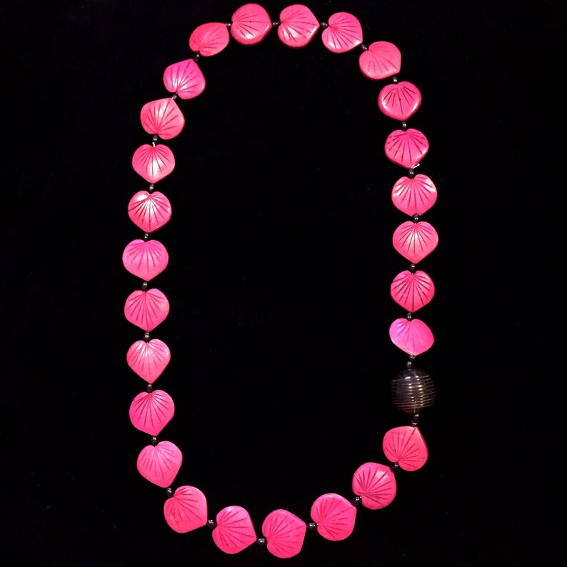 Puede incluir: Un collar de cuentas de coraz&oacute;n rosa con una cuenta de metal oscuro en la parte inferior.
