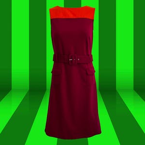 May include: A sleeveless dress with a burgundy bodice and a bright orange top. The dress has a belt with a silver buckle and two pockets on the front.
