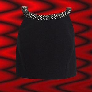 May include: A black top with a jewel-embellished neckline. The sleeveless garment has a simple, elegant design, perfect for evening wear. The top is set against a red and black wavy background.