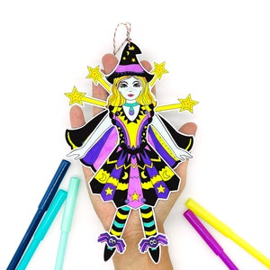 May include: A paper craft witch doll with a purple and yellow dress, black hat, and yellow stars. The doll is holding a wand and has a purple and yellow cape.