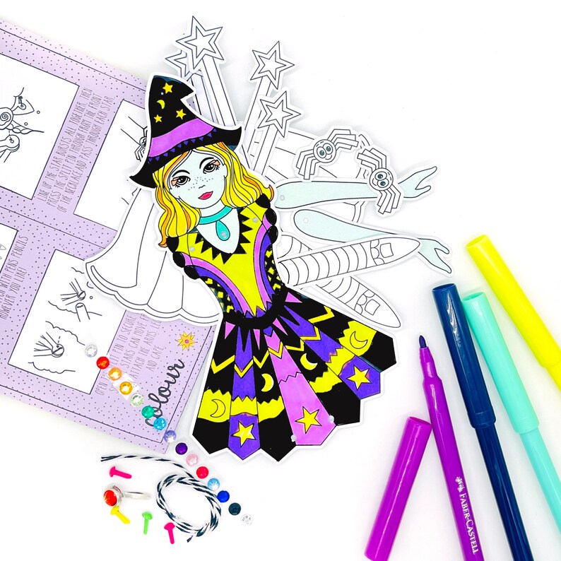 May include: A printable paper doll craft kit featuring a witch with a purple and yellow dress, a pointed hat, and a wand. The kit includes a variety of accessories, such as stars, a spider, and a crescent moon. The kit also includes a string of colorful gems and a set of colored markers.
