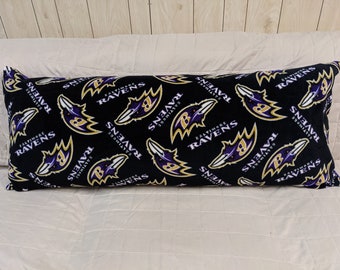 May include: Black body pillow with a repeating pattern of the Baltimore Ravens logo and text in purple, gold, and white. The pillow is rectangular and has a soft, plush appearance.