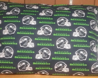 Puede incluir: Una funda de almohada rectangular con un patrón repetido de cascos de fútbol de los Seattle Seahawks y el nombre del equipo en verde y blanco sobre un fondo azul oscuro. La funda de almohada tiene un borde blanco en un lado.