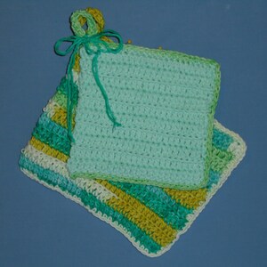 May include: Two handmade crochet potholders. One is solid light turquoise, the other has stripes of turquoise, white, and yellow. A turquoise loop and bow are attached to the top of the solid potholder. The potholders are square and have a textured appearance.